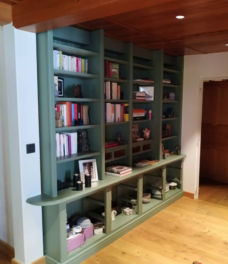 Chalet de Chamonix : bibliothèque murale sur mesure peinte en vert sauge, du sol au plafond à caissons en bois verni, avec plan de travail et niches basses