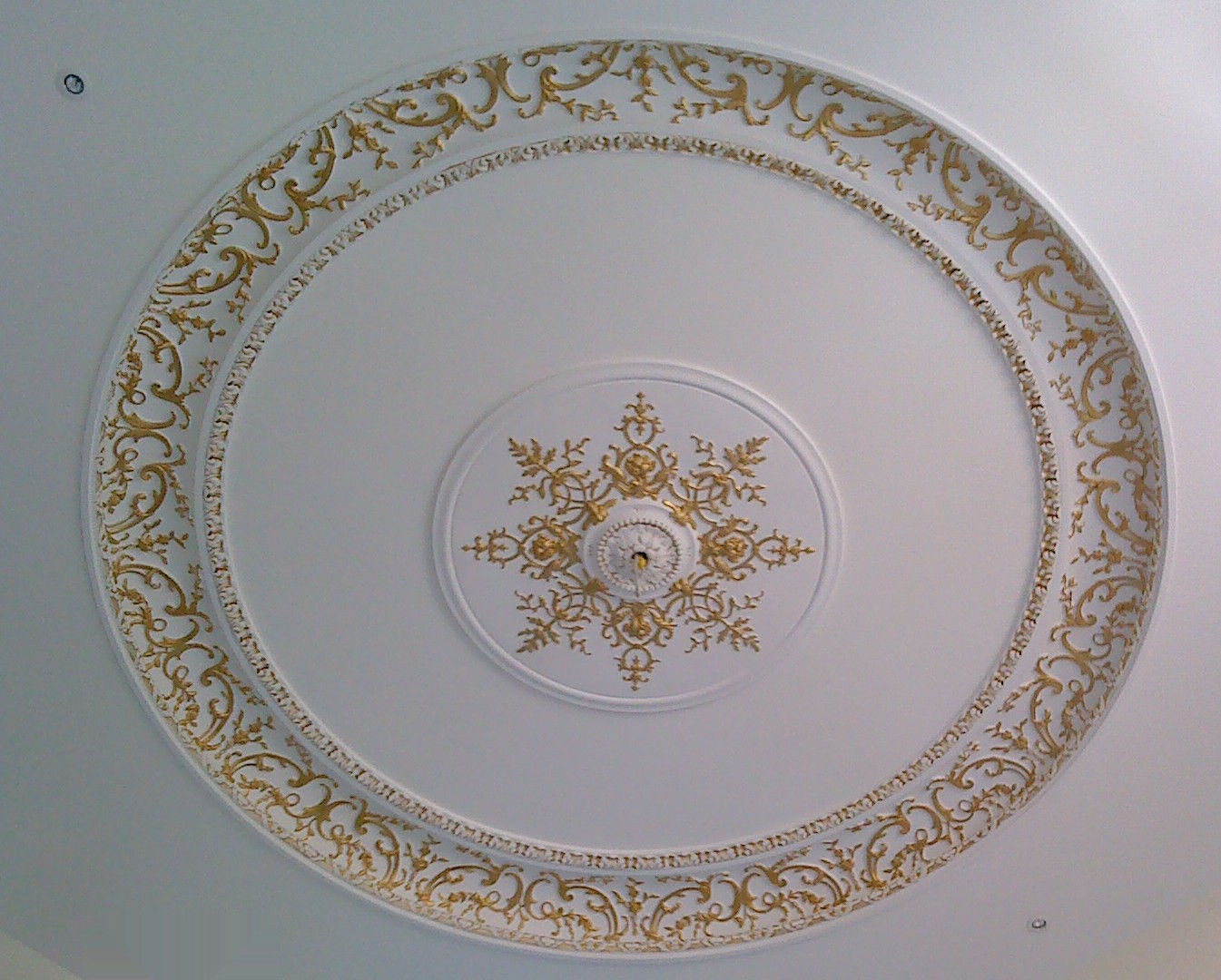 Rosace de plafond en moulure blanche, corniche et couronnes ornées de rinceaux d’acanthes dorés à la feuille d’or, dans une cage d’escalier