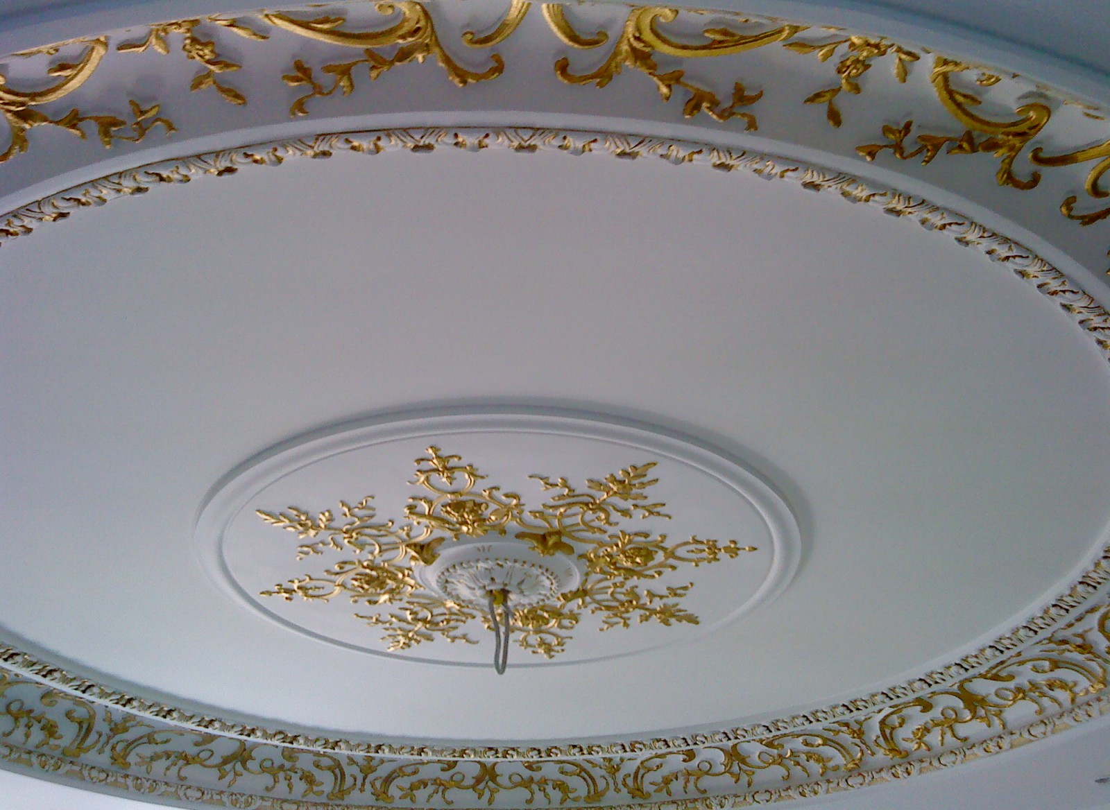 Détail de la dorure à la feuille d’or sur le relief de la moulure : rinceaux, oves et semis floral autour de la sortie de luminaire