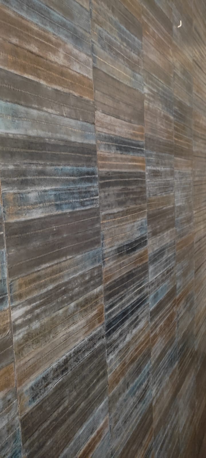Détail du revêtement mural : bandes striées de cuivre, bleu nuit et gris, posées en quinconce